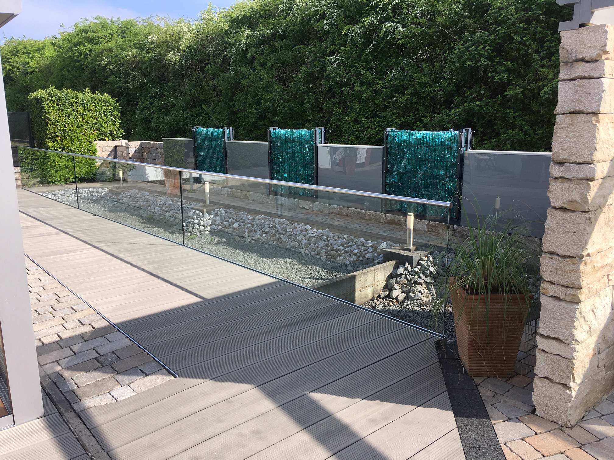 Erhöhte WPC-Terrasse mit Glasgeländer auf Schraubfundamenten als langlebige und betonfreie Fundamentlösung für den Gartenbau.