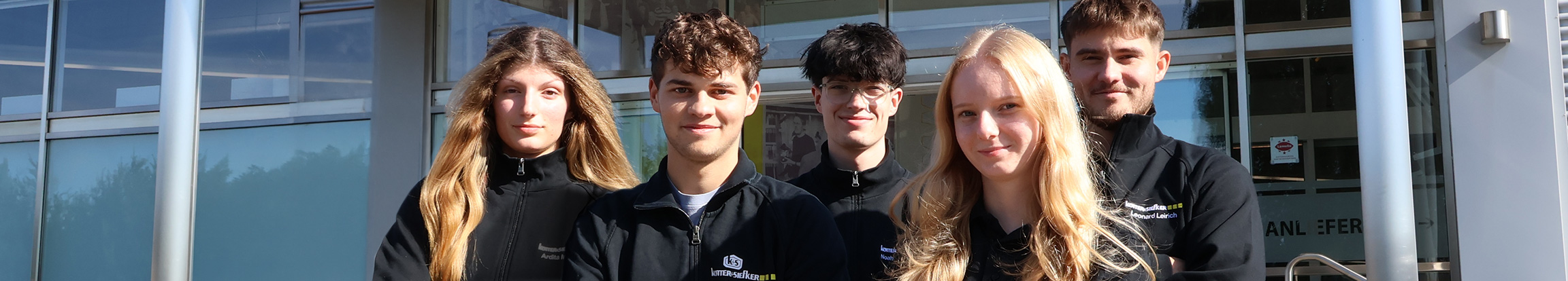 Ausbildung und Karrierestart im Großhandel für Industriebedarf mit engagiertem Nachwuchsteam vor dem Unternehmensstandort. Weitere Zeilen anzeigen