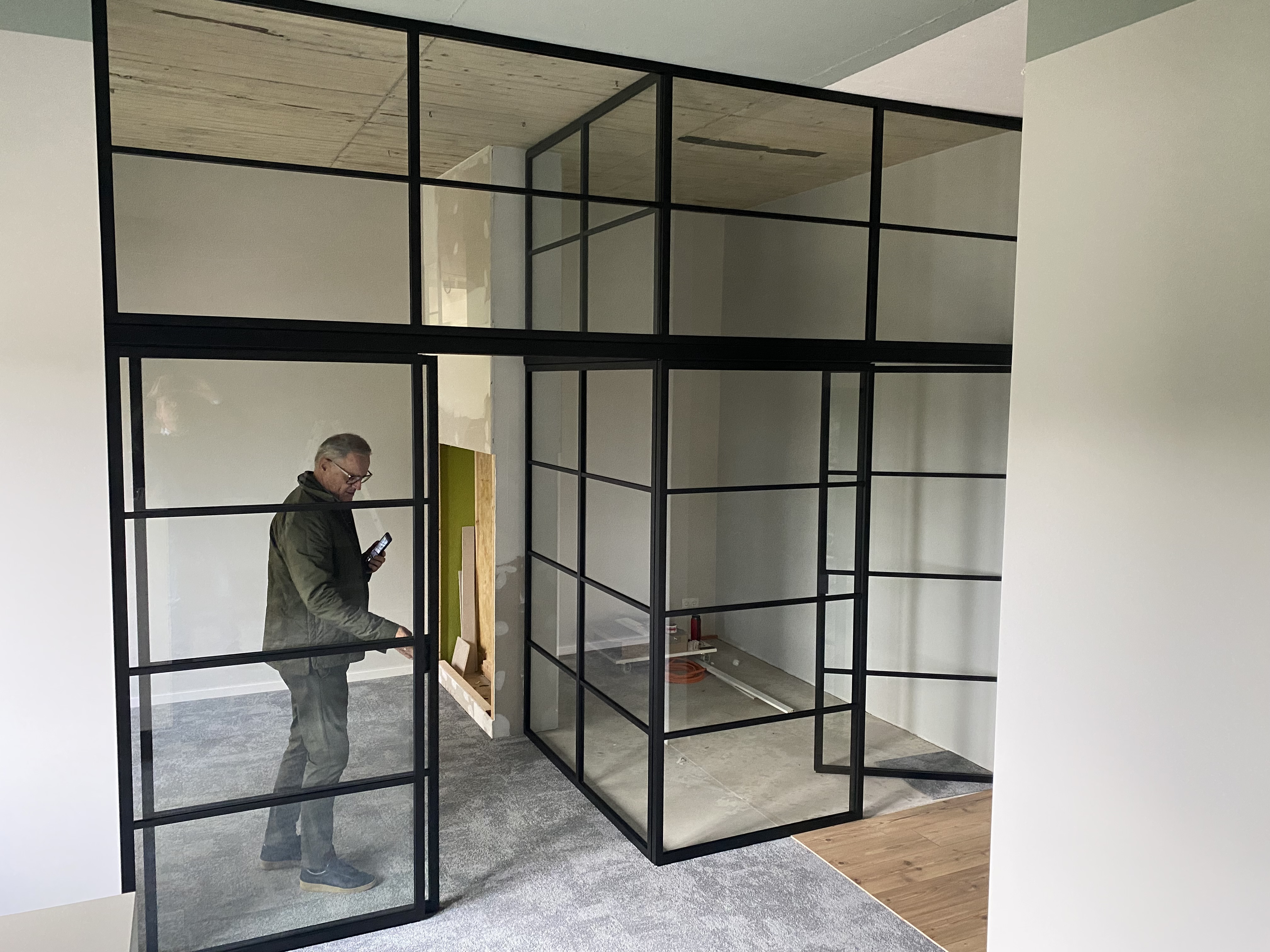 Maßgefertigte Lofttrennwand mit Glaselementen und schwarzen Aluminiumprofilen für offene Wohn- und Arbeitsbereiche.