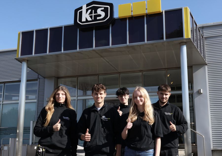6 Auszubildende stehen vor der Verkaufsstelle von Kötter und Siefker und blicken geschlossen in die kamera. Alle tragen einen schwarzen Pullover mit dem Firmenlogo.