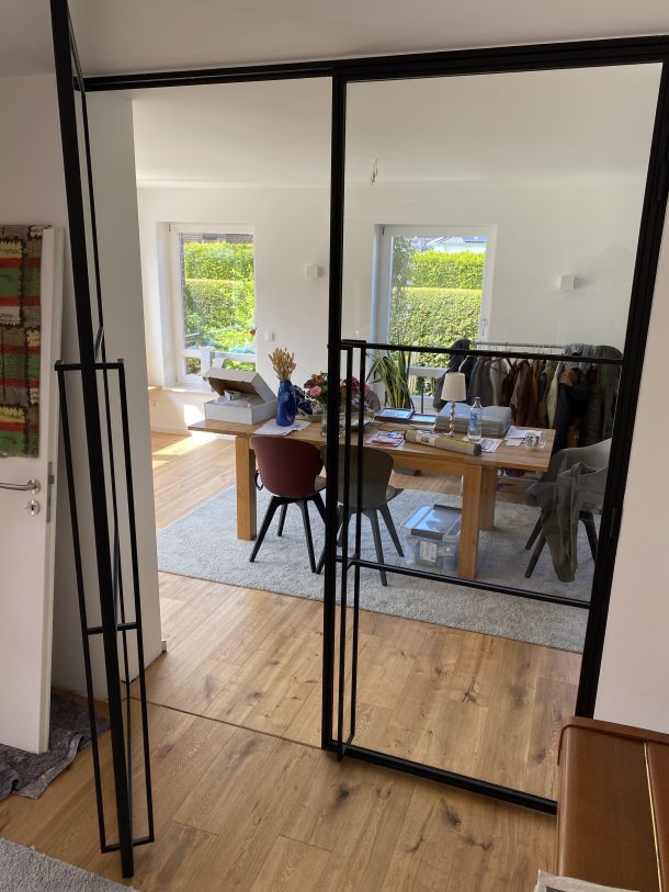 Raumhohe Glas-Trennwand mit schwarzem Stahlrahmen für moderne Innenarchitektur im Industrial Design.